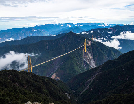 Suspension bridge spanning a deep, forested mountain valley with clouds - Powered by Adobe