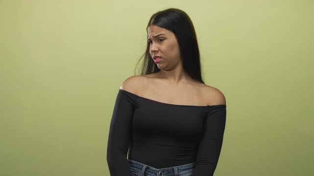 Woman glances to side showing bare shoulder against green wall in studio under soft lighting; disgust.