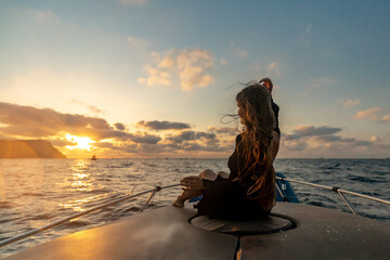 Woman sunset boat. A young woman sits on a boat's bow, gazing at the ocean during a serene golden hour sunset.