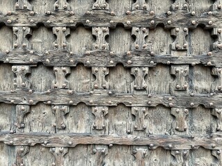 A close-up texture of an old wooden door featuring weathered timber planks and a repeating pattern of metal rivets. he aged surface of historic architecture. 