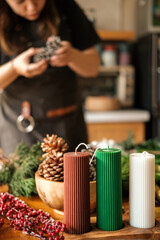 In the foreground are wax candles in Christmas colors. In the background, a young woman creates a...