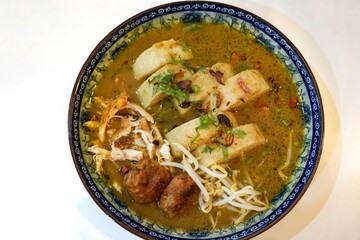 Authentic Soto Ayam served in a decorative bowl with shredded chicken, potatoes, bergedil, bean sprouts, and garnishes in rich chicken broth.