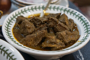 A bowl of rendang hati lembu (beef liver rendang) in thick, dark gravy served in a patterned ceramic bowl with spoon, isolated on white background.