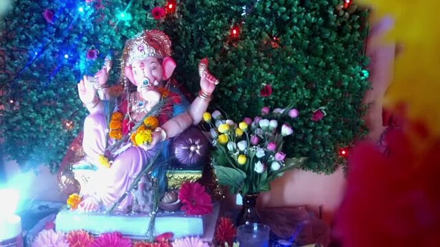 A vibrant close-up of a Ganesha idol features intricate details, with a pearl garland and red hibiscus flowers adorning the deity, symbolizing prosperity and new beginnings.