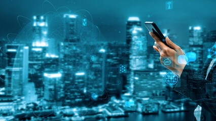 A businessman holds a smartphone against a stunning city skyline at night, emphasizing the integration of technology in urban life with a futuristic digital interface. Xenic
