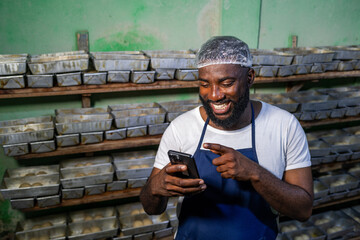 Local African baker, successful small business entrepreneur uses his smartphone for client video calls, online orders, digital banking and social media in his bakery, SME