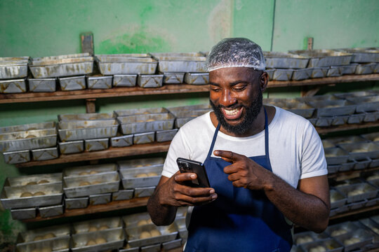 Local African baker, successful small business entrepreneur uses his smartphone for client video calls, online orders, digital banking and social media in his bakery, SME