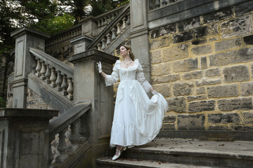 Obraz premium Full length female figure of blonde model wearing white fantasy wedding gown. walking down stairs on historical staircase of fairytale castle location 