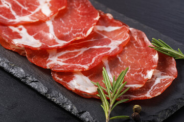 Cured pork coppa slices with rosemary on slate