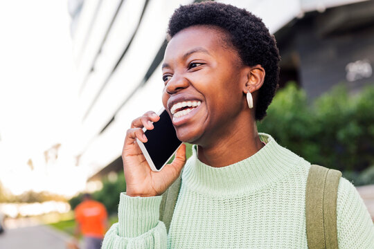 young african american woman with short hair smiling happy while talking on cell phone, concept of technology of communication and modern lifestyle