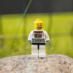 Naklejka premium Lego astronaut figure standing on a rock with a blurred green background