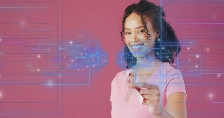 Presenting African American woman holding pink ribbon in studio, with digital overlay, copy space