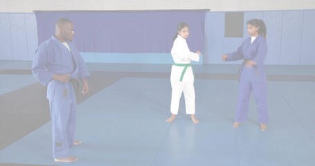 Directing instructor in blue gi guiding students sparring in dojo on foam mats, with colored belts