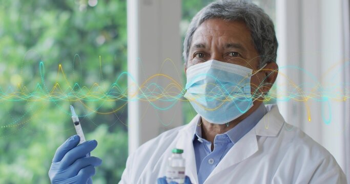 Senior doctor wearing lab coat, mask, gloves holding syringe, vial beside clinic window, copy space
