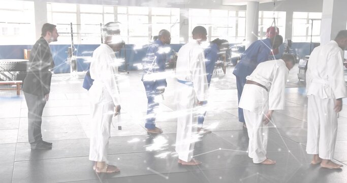 Coach wearing suit and group in gis lining up facing right in dojo, with colored belts