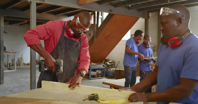 Drilling carpenter in red shirt securing plank at workshop bench, with cordless drill, copy space