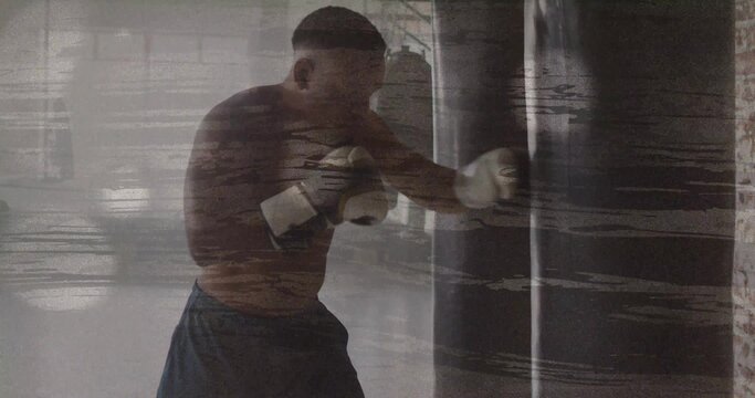 Striking boxer delivering punch to heavy punching bag inside gym, with white gloves and dark shorts