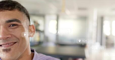 Smiling man in purple shirt facing camera in open-plan office with play-pin-chat badges, copy space