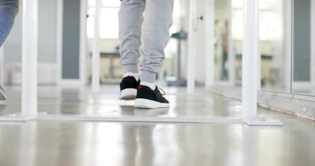 Walking adult male wearing grey sweats, white socks, black sneakers in studio with mirror, barre