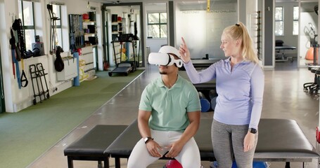 Guiding instructor in purple coaching client seated on padded bench wearing VR headset at rehab gym