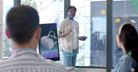 Standing man holding tablet and gesturing in modern office, VR monitor, glass board, striped shirt