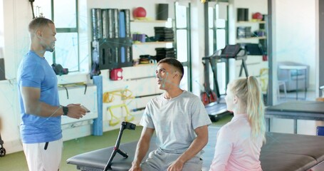 Consulting therapist in blue shirt holding tablet with seated patient on treatment table, crutch