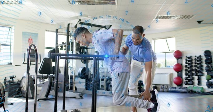 Doing dip client leaning forward over dip bars in gym, trainer supporting ankle wearing gym gear - Powered by Adobe