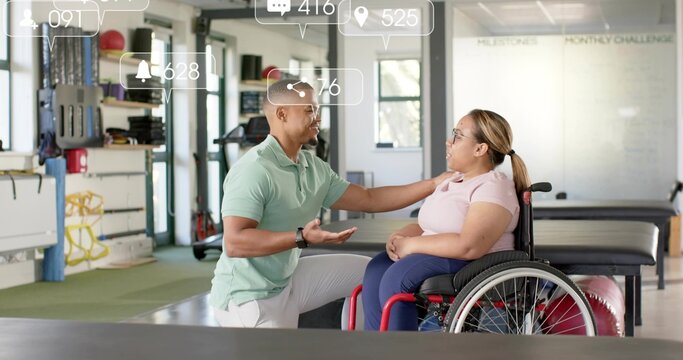 Kneeling therapist placing hand on woman in manual wheelchair at therapy gym, wearing green polo