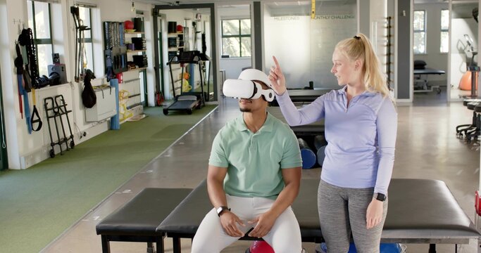 Guiding instructor in purple coaching client seated on padded bench wearing VR headset at rehab gym - Powered by Adobe