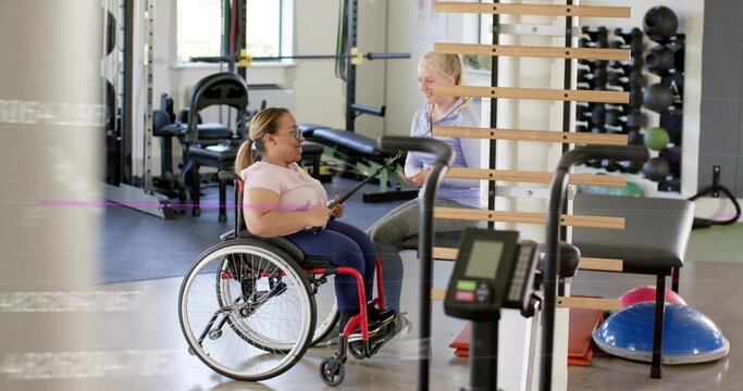 Pulling resistance band woman in manual wheelchair in pink top exercising at gym, coach with tablet