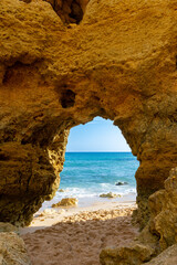 A naturally formed sandstone arch dominates the frame, perfectly framing the azure Mediterranean Sea in a striking contrast of golden rock and blue water