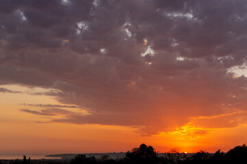 A sliver of land anchors the glowing horizon beneath a canopy of clouds and fading sunlight