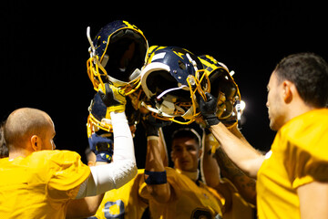 Football players raising helmets celebrating victory at night