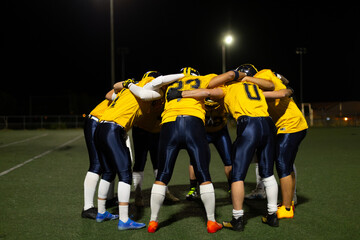 American football team huddling on field at night