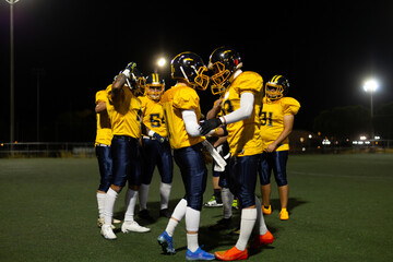 American football players huddling on illuminated field at night