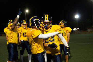 American football players celebrating victory on illuminated field at night