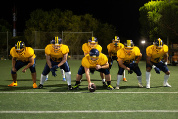 American football players preparing for scrimmage on field at night