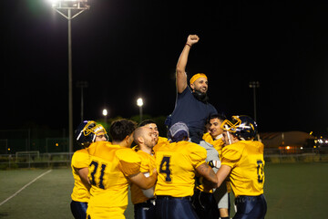 American football team celebrating victory carrying coach on shoulders