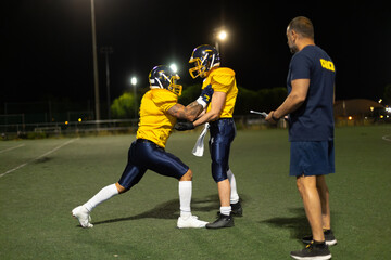 American football players training with coach at night
