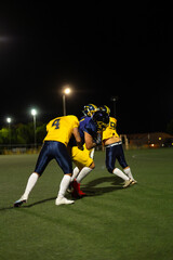 Football players tackling during night game on green field
