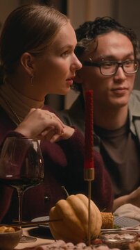 Vertical shot of bicultural couple of man and woman sitting at festive table during Thanksgiving celebration and communicating