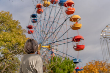 Ferris wheel amusement park woman looking at colorful ride in an autumn park