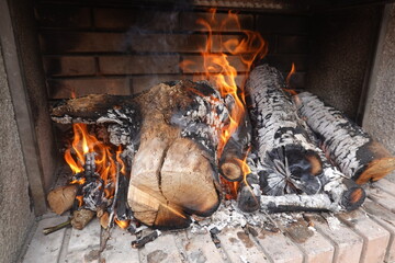 Burning firewood slowly consumed by fire in brick fireplace