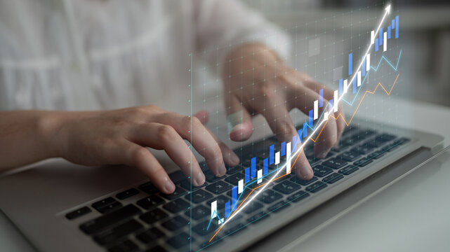 A person hands are typing on a laptop keyboard, with digital financial graphs and charts illustrated above, showcasing growth and analysis in a modern workspace. Impute