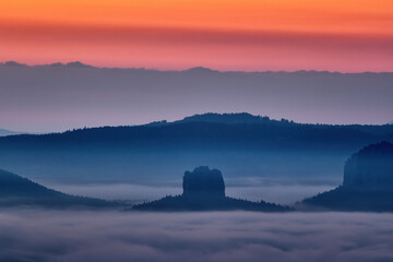Misty sunrise over the Lilienstein table mountain in Saxon Sächsische Schweiz, Germany autumn landscape. Travel in Europe. Misty foggy morning sunride in nature. Rock hills with trees and forest.