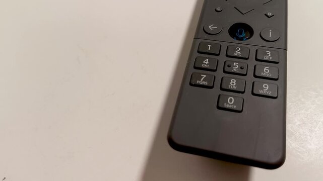 Sleek modern remote control with voice command button and numeric keypad rests on a clean white surface, hinting at seamless home entertainment interaction and smart device control.