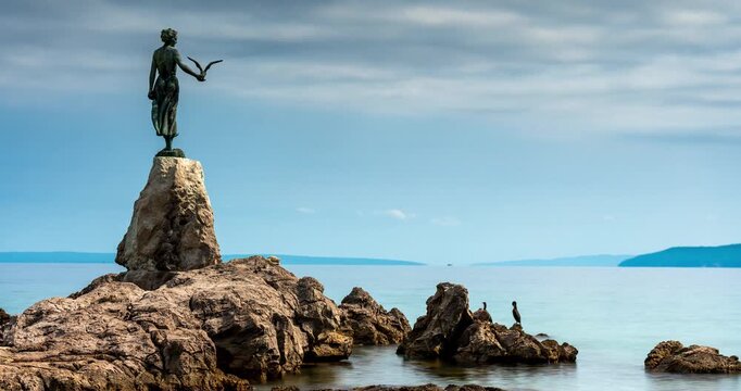 Opatia, Croatia - August 20, 2025: Timelapse. A calm seascape, featuring the iconic “Maiden with the Seagull” statue standing gracefully on a rocky shore under a moody blue sky - Powered by Adobe