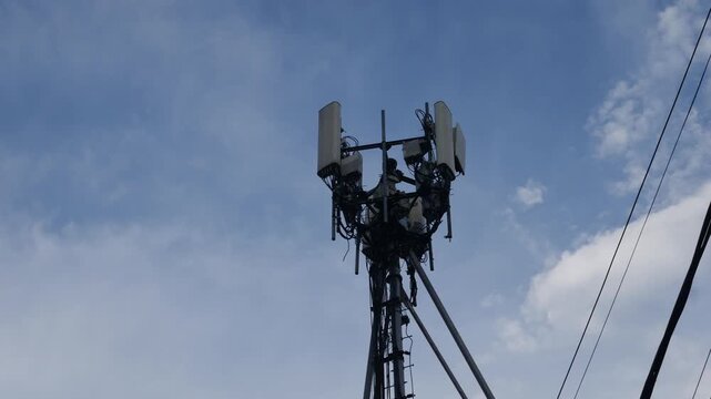 Cellular telecommunications tower with antennas and equipment against blue sky with white clouds and power lines