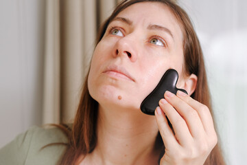 40s woman takes care of her face skin in the morning. She doing massage treatment for tensions with Gua Sha tool. Self facial care. Wellness, beauty and skincare routine. Healthcare projects