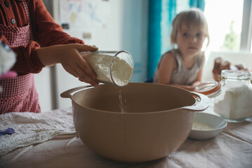 Child pouring flour into bowl while baking in home kitchen with friend